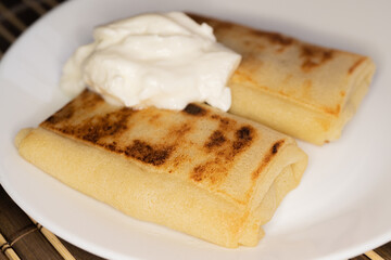 Home kitchen. Pancakes with sour cream on a white plate