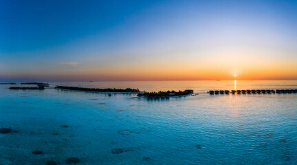Maldives, Helicopter view of tourist resort bungalows stretching along coast of Maadhoo island at sunset