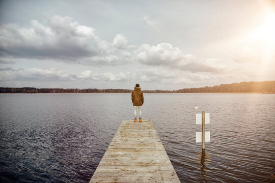 Back view of young man standing on a jetty looking at lake