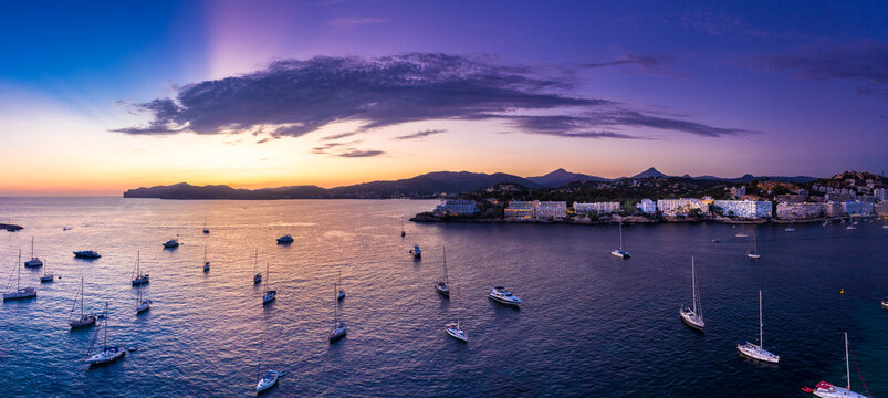 Spain, Mallorca, Santa Ponsa, Aerial panorama of boats floating in coastal water at purple dusk with town in background