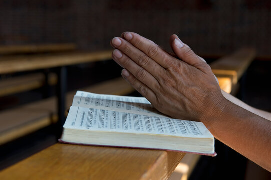 Praying hands on hymnbook on pew