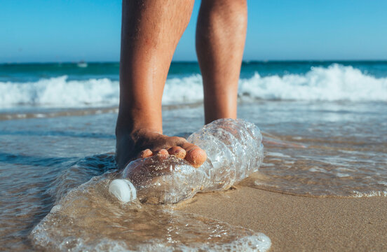 Foot of man stepping on empty plastic bottle lying on the beach, close-up