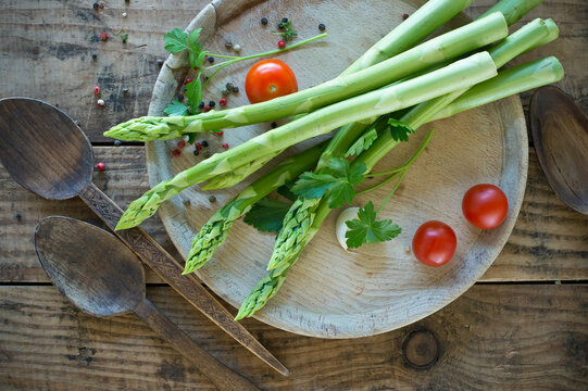 Two wooden spoons and tray with fresh asparagus, cherry tomatoes, parsley and pepper