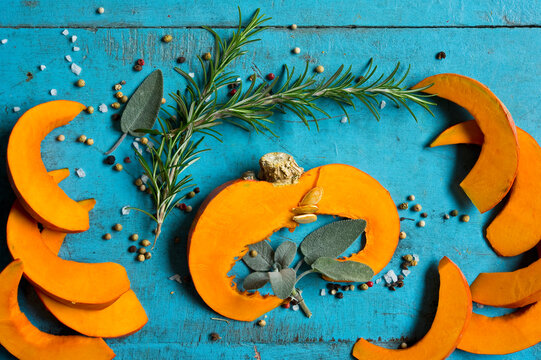 Slices of red kuri squash (Cucurbita maxima), rosemary, sage, salt and pepper lying on blue cutting board