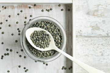Jar of green lentils on wooden table seen from above