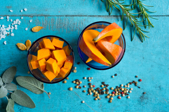 Bowls of red&Ocirc;&oslash;&Omega;kuri&Ocirc;&oslash;&Omega;squash&Ocirc;&oslash;&Omega;(Cucurbita&Ocirc;&oslash;&Omega;maxima) slices, rosemary, sage, salt and pepper lying on blue cutting board