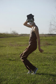 Portrait of young man with white face paint dancing on a meadow
