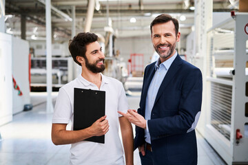 Portrait of smiling businessman and employee with clipboard in a factory