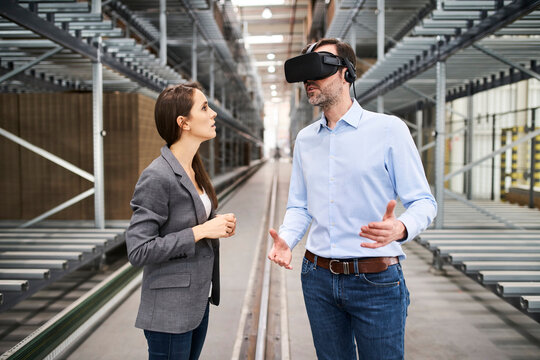 Businesswoman talking to businessman wearing VR glasses in factory