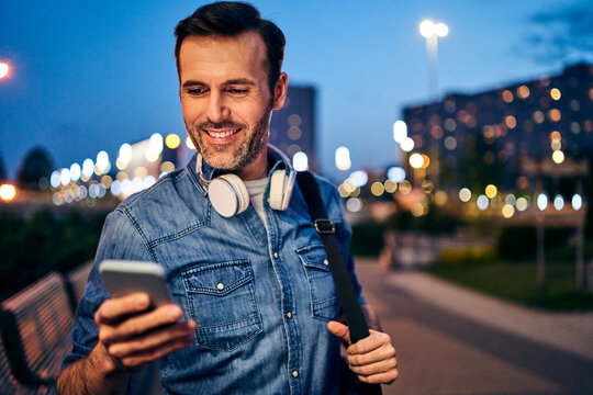 Smiling man using his smartphone in the city in the evening