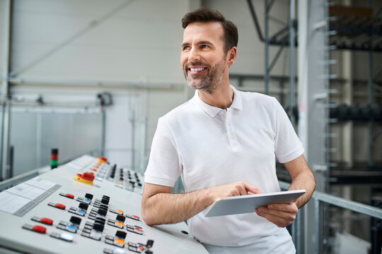 Smiling man using tablet at control panel in a factory