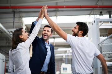 Happy businessman and employees high fiving in a factory