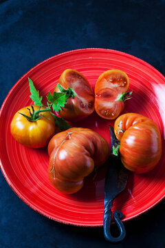 Whole and sliced beef tomatoes 'Chocolate Stripes' on red plate