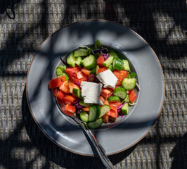 Summer healthy food served outdoor in sunlights, vegetable greek salad made with fresh cucumber, tomatoes, onion, feta cheese