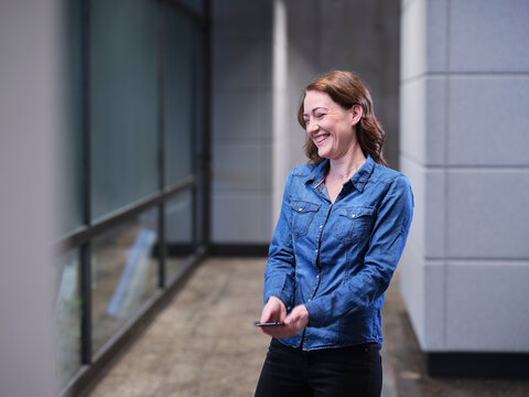 Laughing businesswoman using cell phone on modern office floor