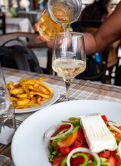 Dinner with white wine in Greek taverna, vegetable greek salad, fried potatoes