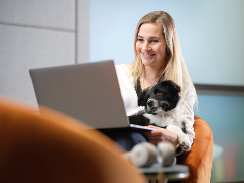 Businesswoman with dog sitting in armchair using laptop
