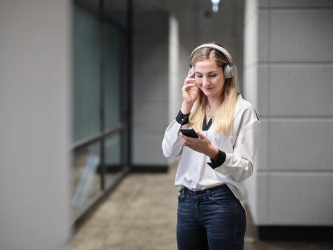 Smiling businesswoman with headphones and cell phone in modern office