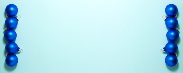 Blue Christmas balls on blue background on left and right side. Flat lay top view with copy space. Holidays concept.