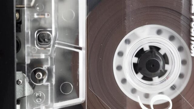 Audio cassette's tape reeling in an old audio recorder. The capstan and the pinch roller on the left side. Macro video of a rotating tape. 