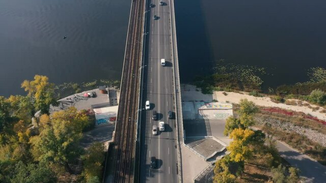 Aerial view. Traffic on the road bridge. Cars and trucks are moving on a concrete bridge over a small river at sunny clear day. Bridge over the Dnepr