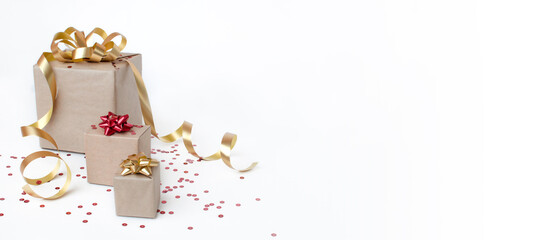 Christmas greeting card composition. Craft paper gift with gold and red ribbon on white background with confetti. 