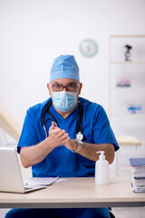 Old male doctor working in the clinic during pandemic