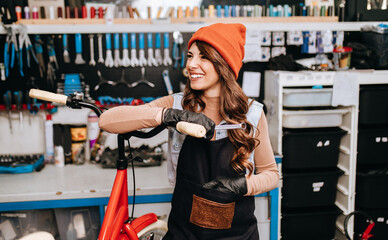 Beautiful young female mechanic enjoying while repairing bicycles in a workshop..