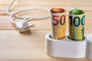 Euro money banknotes inserted into a white extension socket on a wooden surface. Expensive energy...
