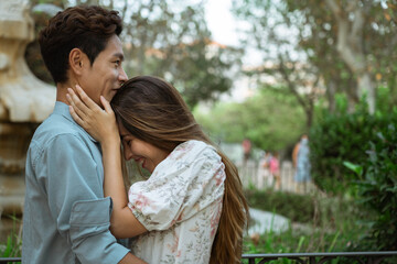 ATTRACTIVE MULTICULTURAL COUPLE HUGGING AT THE PARK, KOREAN MAN AND EUROPEAN WOMAN