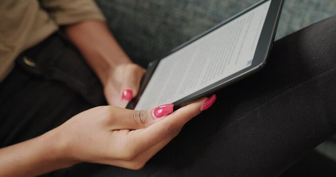 Female student reading ebook and lying on sofa. Young African American woman relaxing with electronic book. Black people and lifestyle with ereader at home. Close-up shot of screen and hands