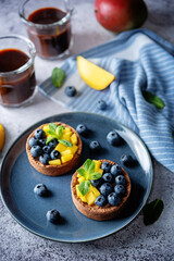 Chocolate tartlets with chocolate cream filling and mango fruit with blueberries