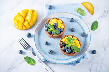 Chocolate tartlets with chocolate cream filling and mango fruit with blueberries