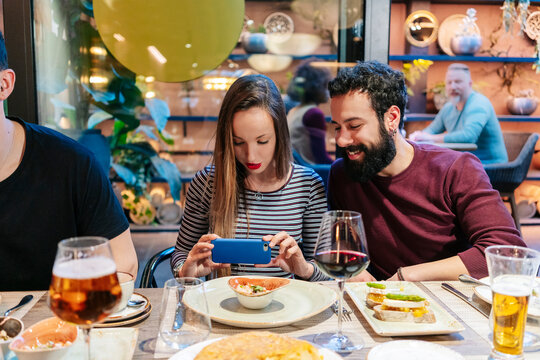 Woman taking smartphone pictures of food at a dinner with friends in a restaurant