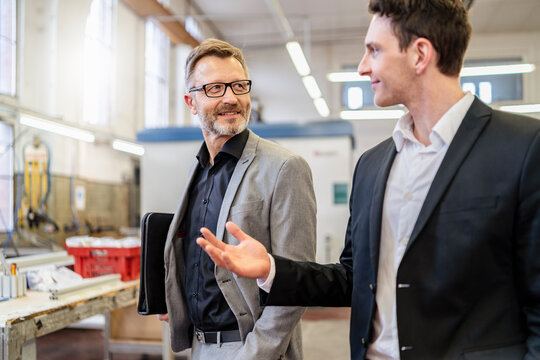 Two smiling businessmen talking in a factory