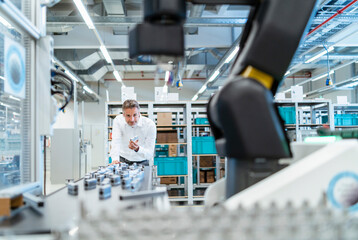 Businessman in a modern factory hall looking at robot
