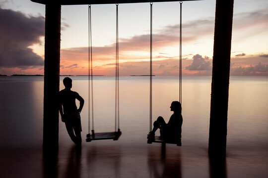 Couple on a swing at the sea at sunset, Maguhdhuvaa Island, Gaafu Dhaalu Atoll, Maldives