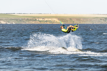 Obraz premium Young adult caucasian fit male person enjoy riding kite surf board making extreme trick stunt bright sunny day against blue sky at sea or ocean shore. Watersport adrenaline fun adventure acitivity