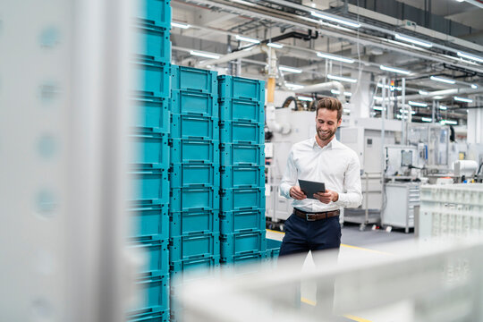 Smiling businessman using tablet in a factory hall with boxes