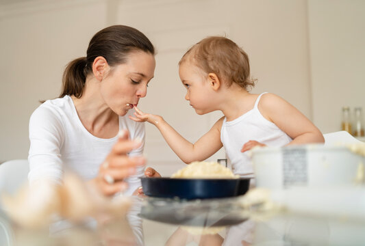 Little girl feeding mother while making a cake in kitchen at home