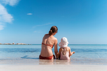 Rear view of mother with daughter sitting in the sea