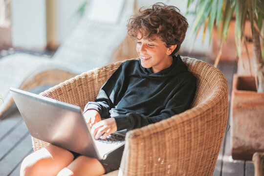Smiling boy sitting in wicker chair using laptop