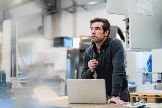 Portrait of a pensive businessman with laptop in a factory