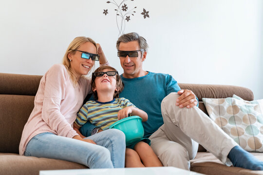 Father, mother and son wearing 3d glasses on couch at home watching Tv