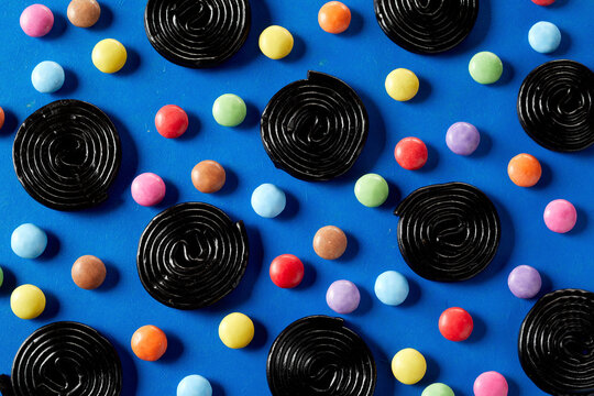 Spirals of liquorice interspersed with colorful sugar-coated chocolate candy on blue background