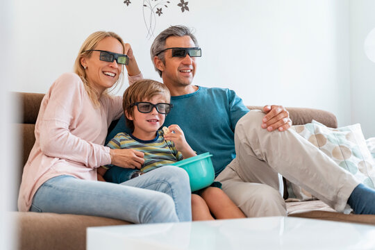 Father, mother and son wearing 3d glasses on couch at home watching Tv