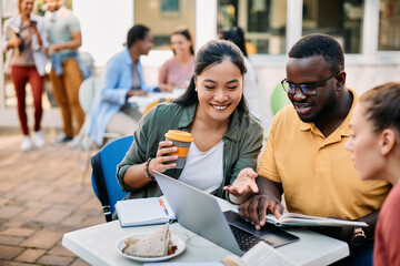 Multi-ethnic group of university students use laptop while learning on lunch break.