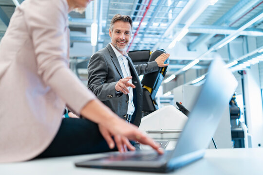 Businessman and businesswoman with laptop and robot in a modern factory hall
