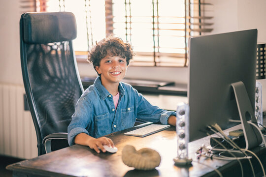 Portrait of smiling boy sitting at desk at home using personal computer