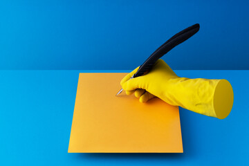 Quill pen held in hand and writing on orange paper over blue background